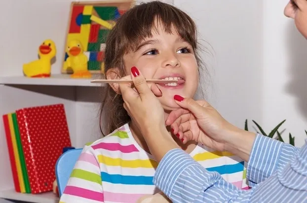 Child receiving throat examination with tongue depressor.