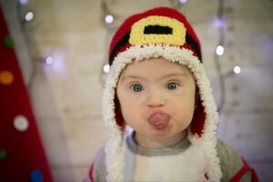Adorable baby wearing a cozy Santa hat, sticking out their tongue playfully.